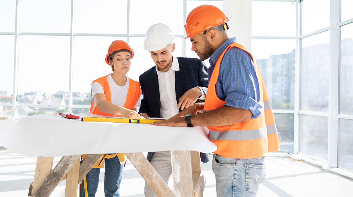 Three construction professionals collaborating on a renovation project, using tools and discussing plans in a bright, modern workspace.